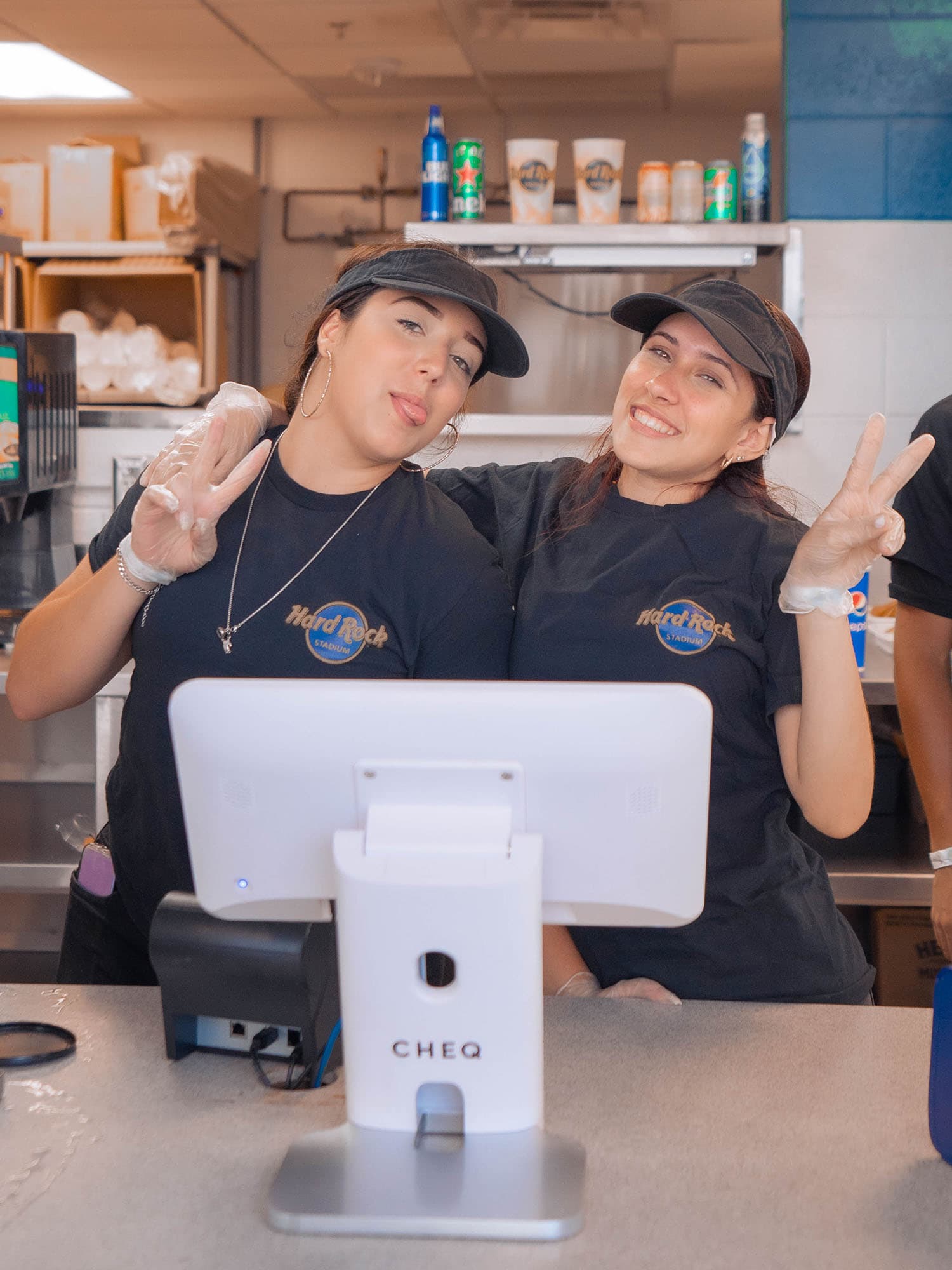 Two workers displaying peace signs in behind CHEQ Point of Sale Kiosk